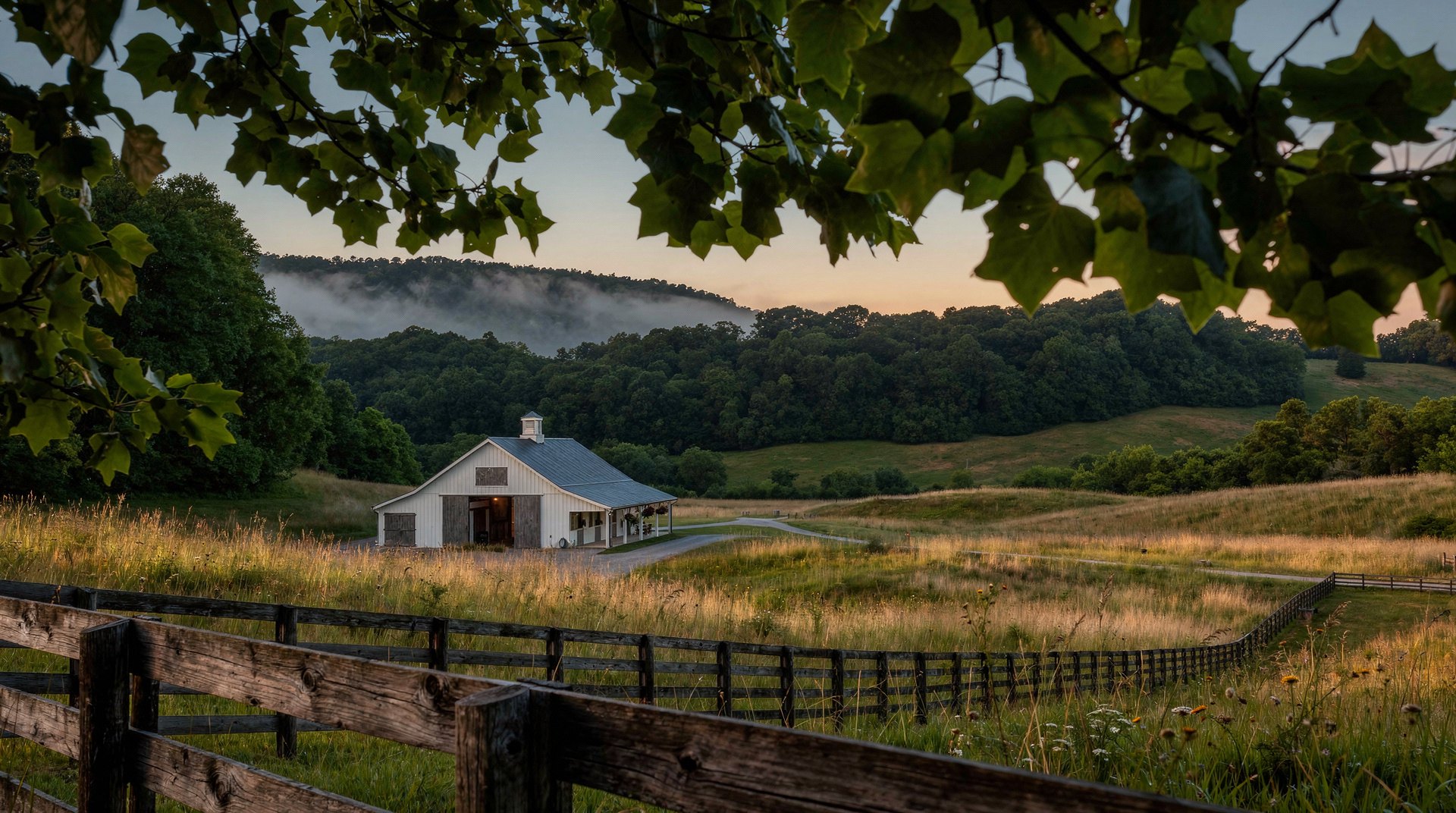 Fenced hay meadow and barn at dusk beneath a wooded ridge in Williamson County, Tennessee